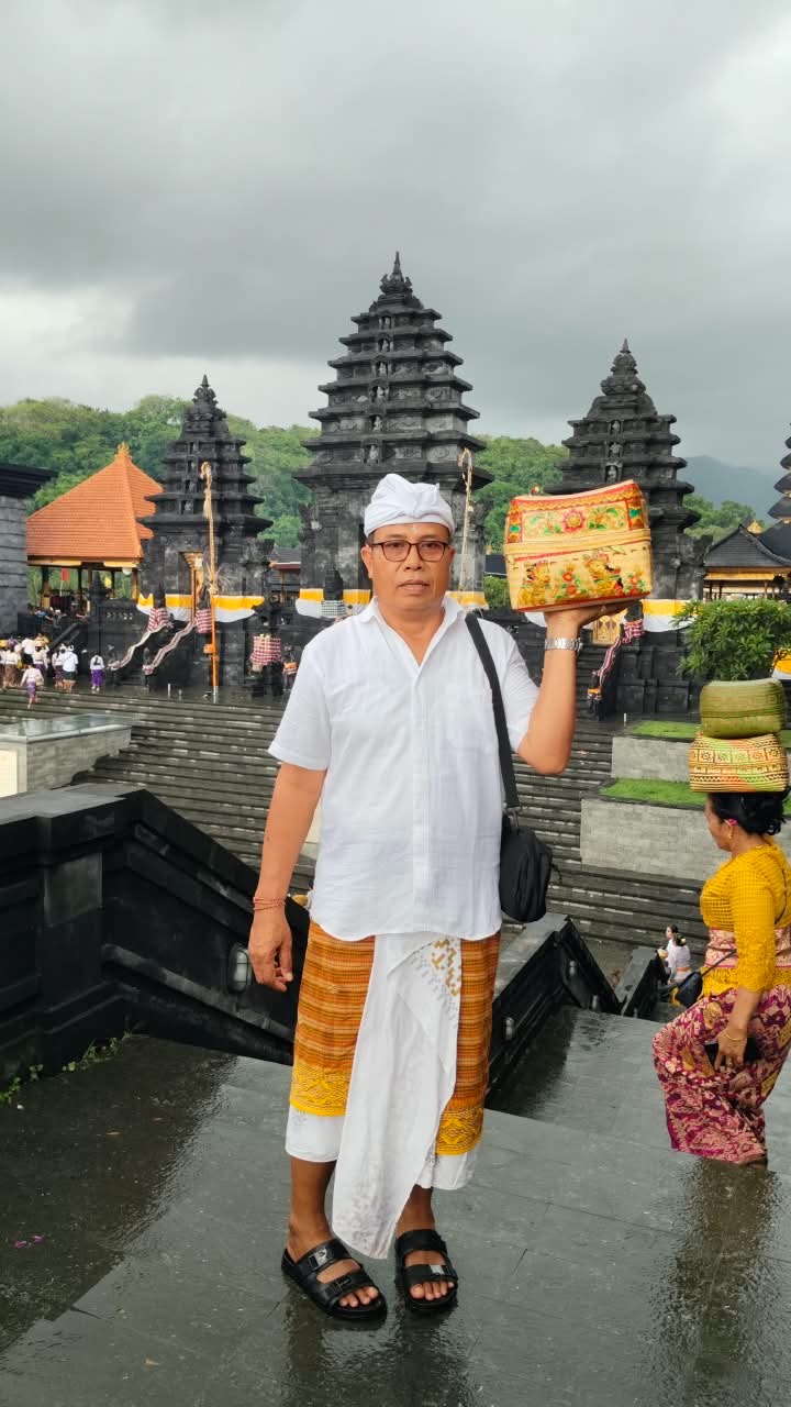 Guide in Balinese ceremonial dress at a temple, holding an offering