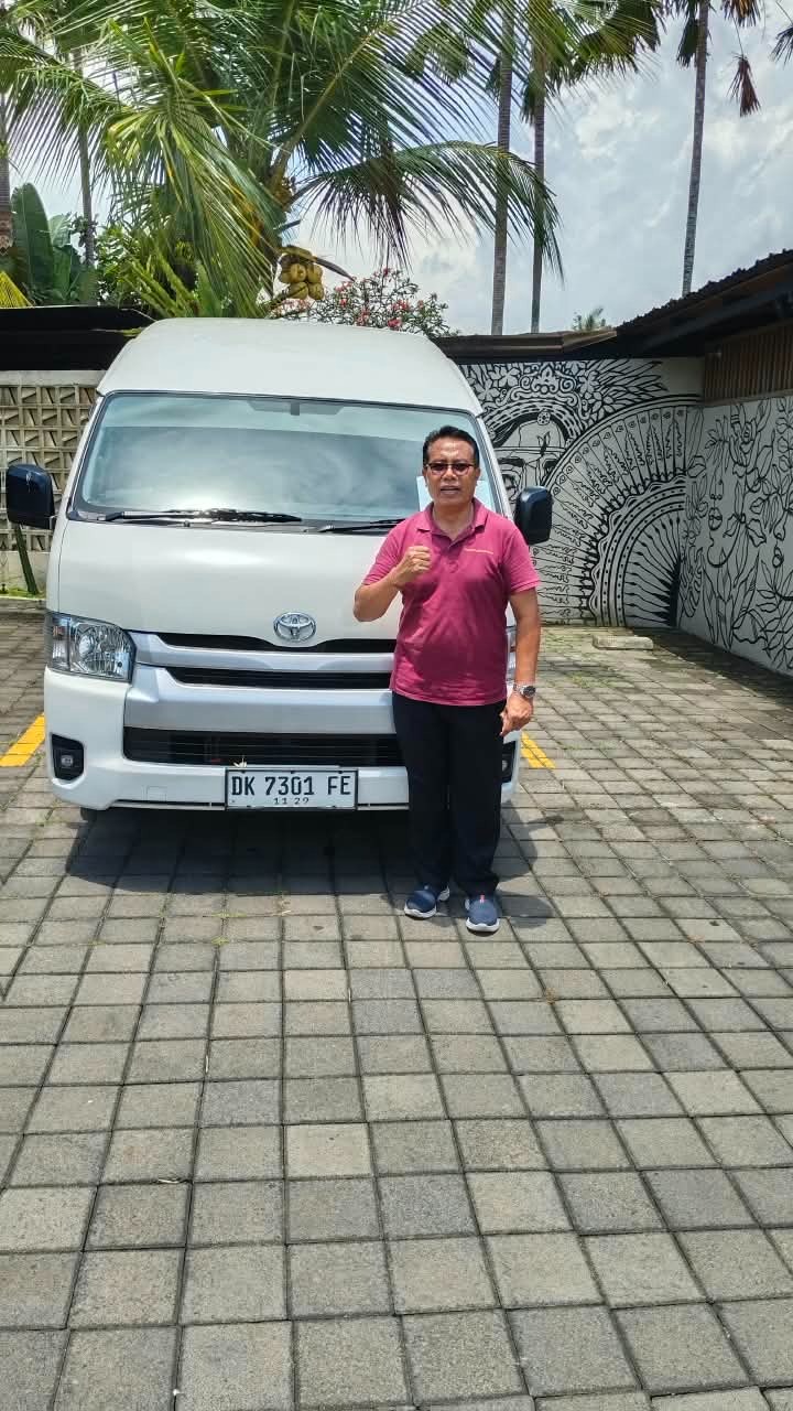 Driver standing beside a white Toyota HiAce van in Bali