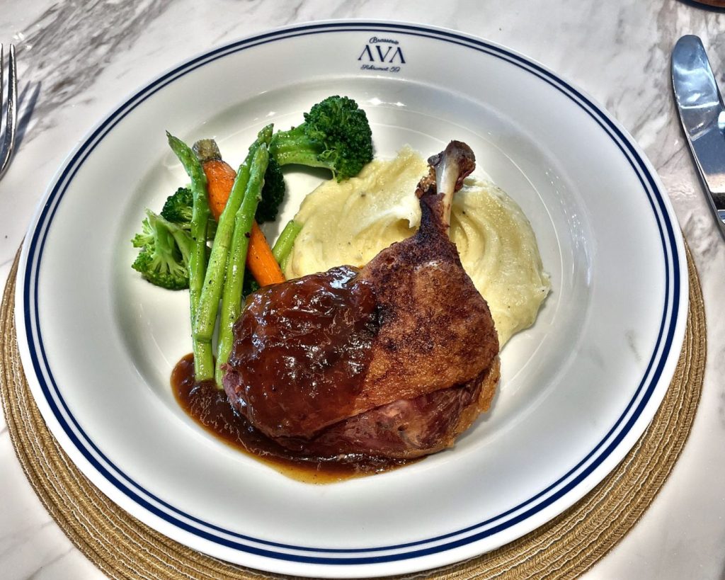 Duck confit with mash and greens on a navy-rimmed plate at AVA Brasserie